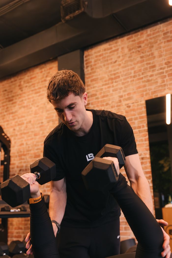 Trainer spotting a client lifting dumbbells
